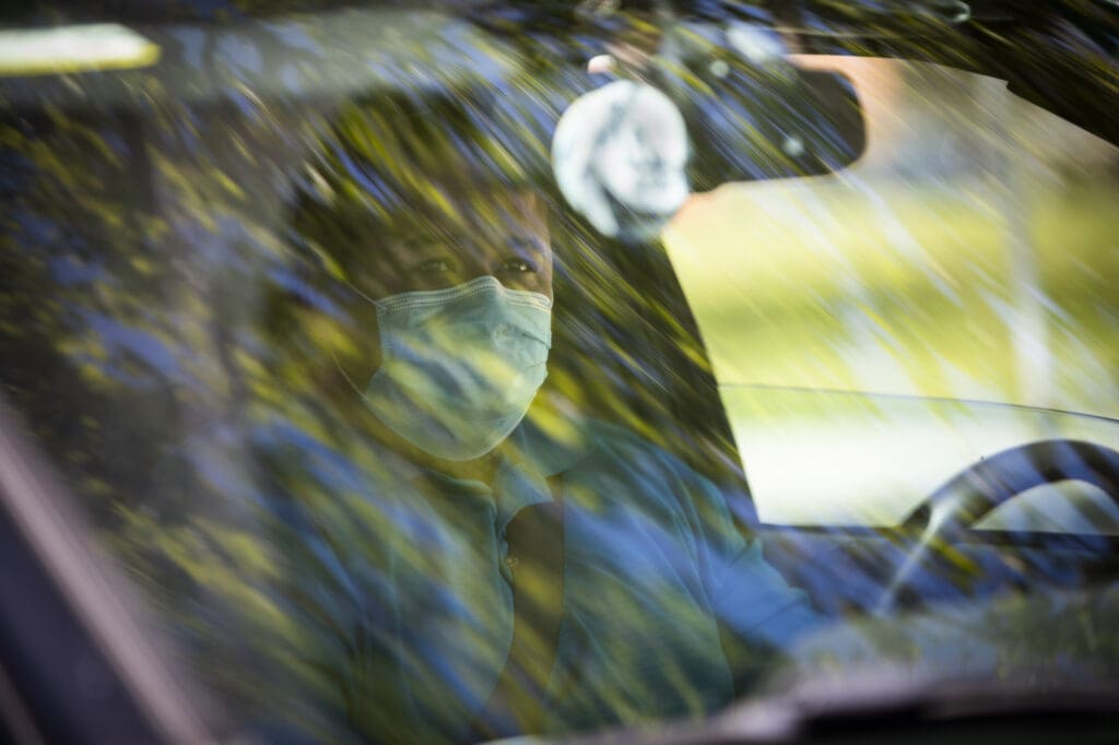 A man in a face mask waits in his car as his trunk is packed with produce and eggs at the Farm Box Program.