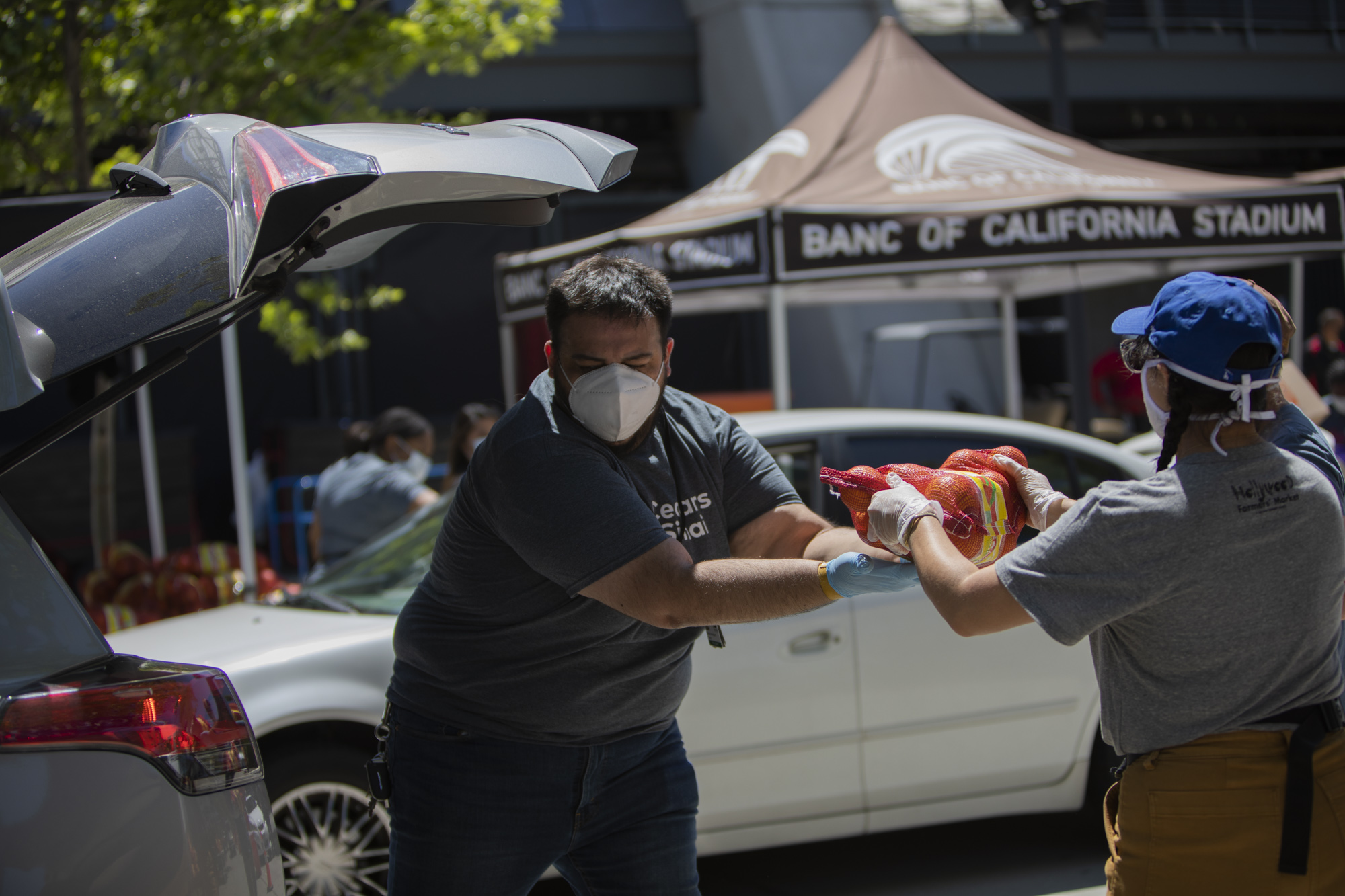 Henry Aguilar, from the Kerlan-Jobes Institute at Cedars-Sinai, is passed a 10-pound bag of oranges to pack into the trunk of a vehicle at the Farm Box Program distribution event.